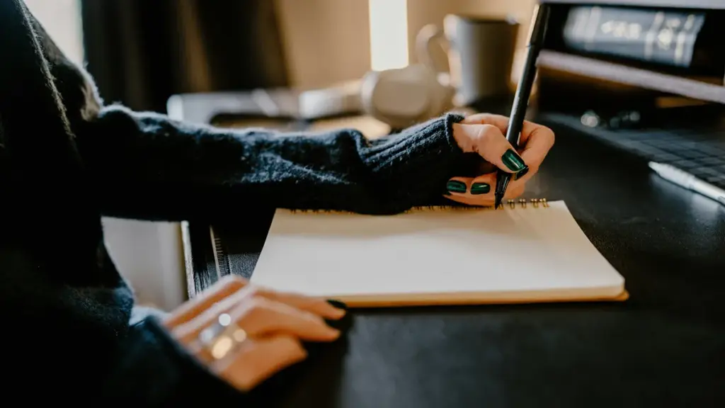Person writing with black pen in notebook at desk workspace