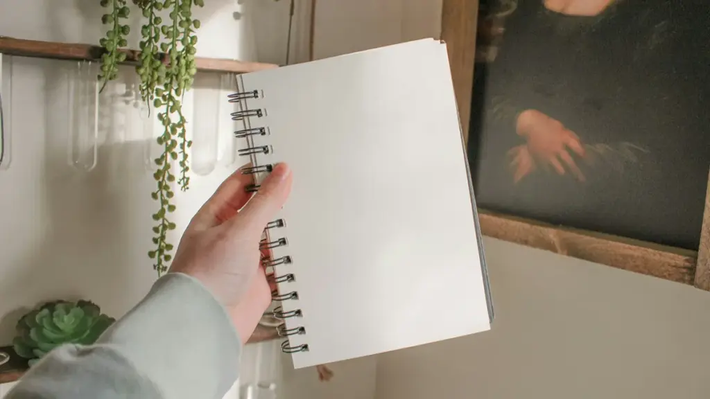 A hand holding an empty spiral notebook in a room