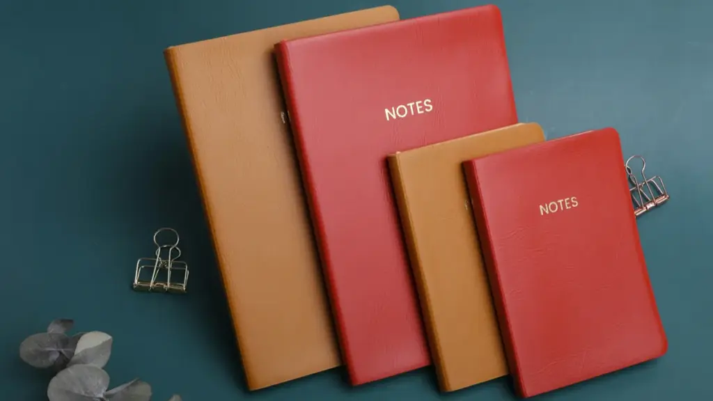 Four stacked red and brown leather notebooks on teal background