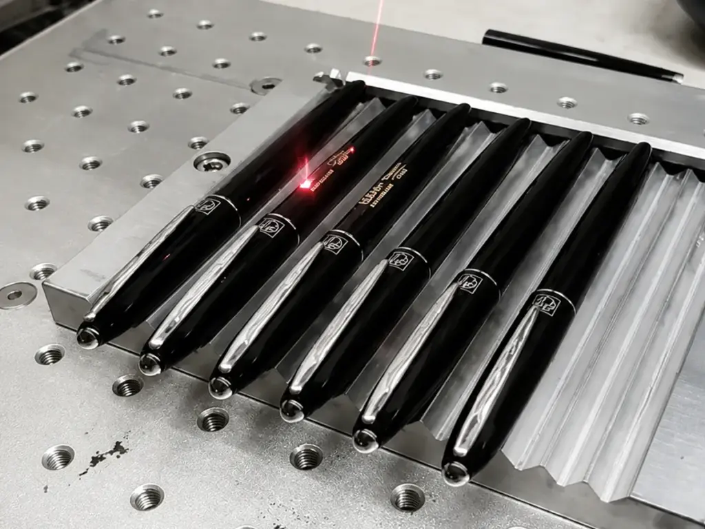 Red laser beam engraving logos on sleek black metal pens