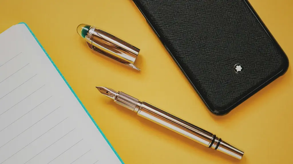 Silver fountain pen beside notepad on bright yellow surface