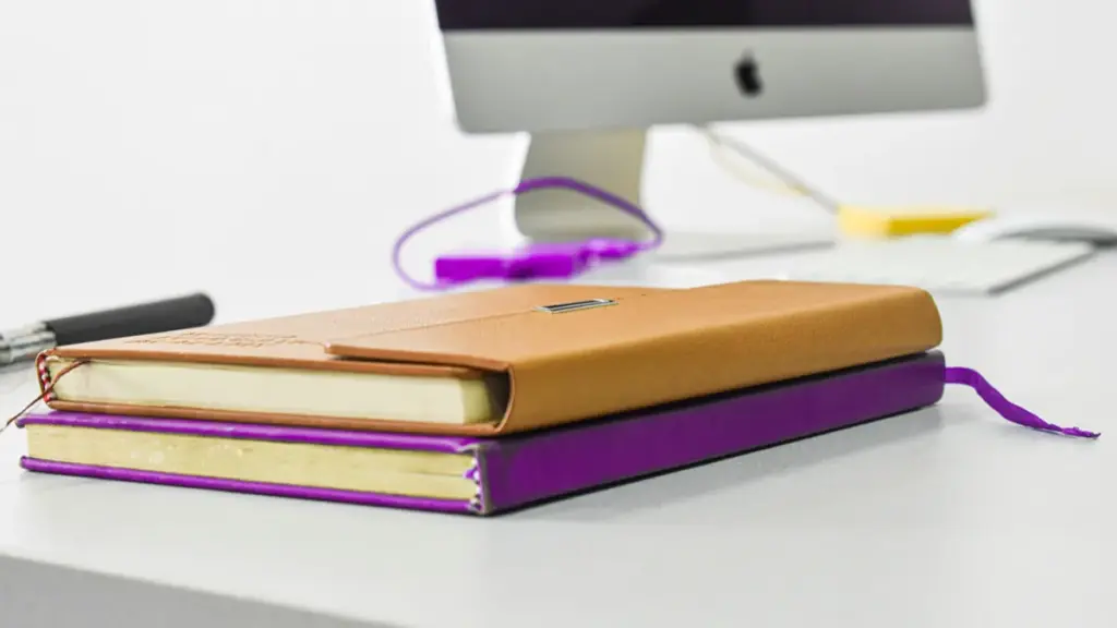 Two closed leather notebooks stacked on a desk near a computer
