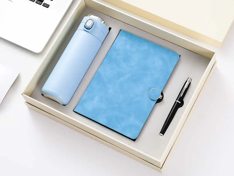 Blue insulated water bottle, notebook, and pen in a gift box on a white desk.