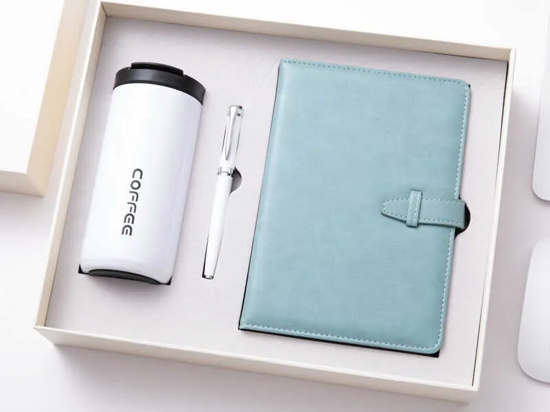 White coffee travel mug, pen, and blue notebook in a gift box