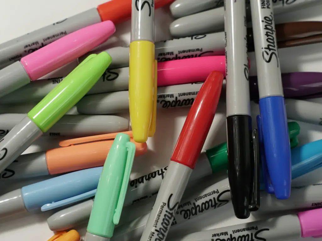 A pile of multicolored Sharpie permanent markers scattered on a white surface.