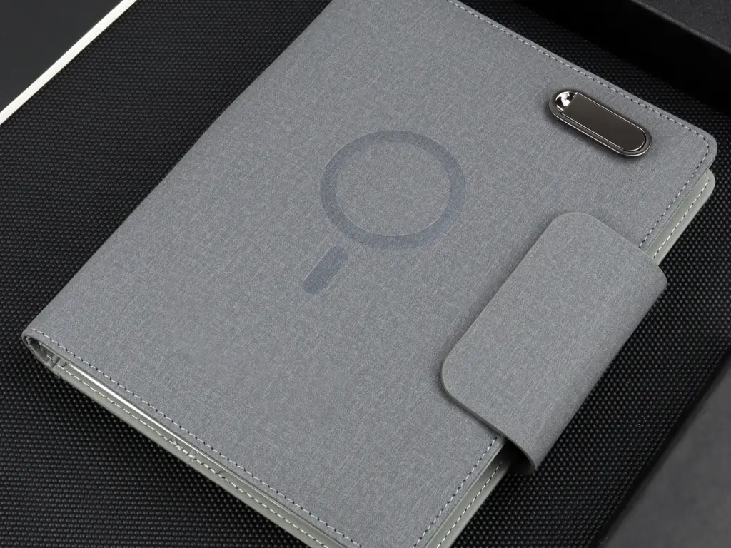Closed gray fabric wireless charging notebook with a charging zone mark, magnetic strap, and metal clip