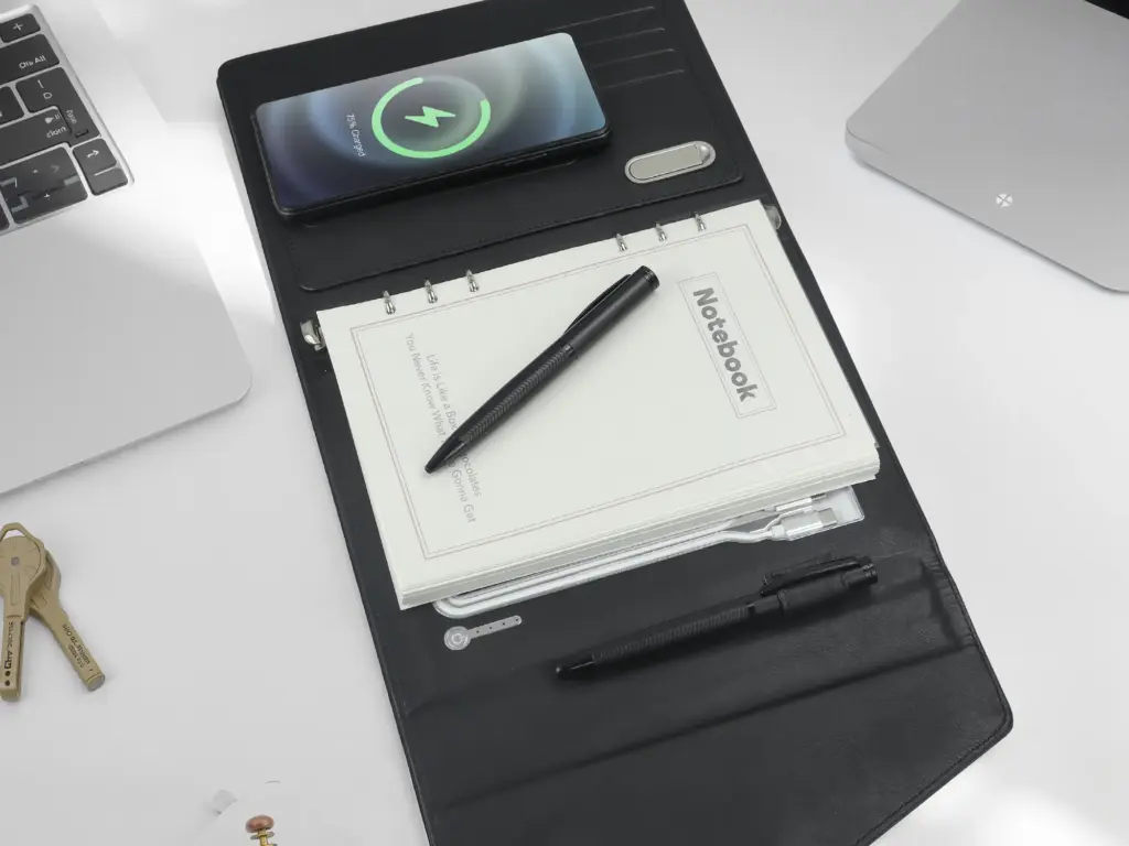 Black leather folio organizer with wireless charging pad, notebook, and pen slots on a desk.