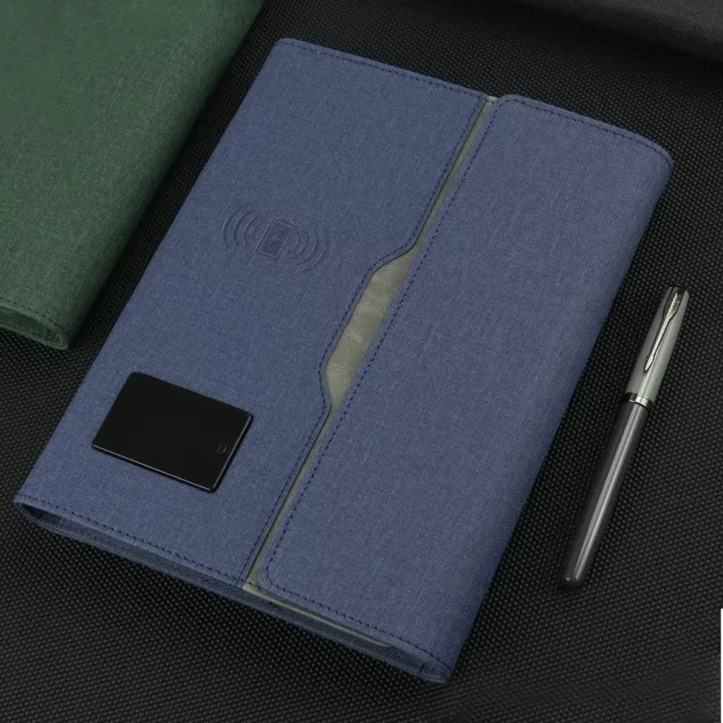 Blue fabric portfolio notebook with wireless charging feature, NFC card slot, and included pen on textured surface