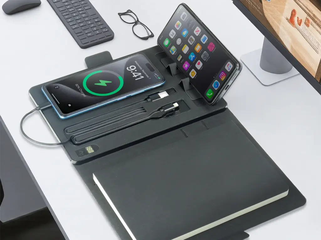 Black wireless charging desk organizer pad with dual phone stands, cable slots, and notebook space.